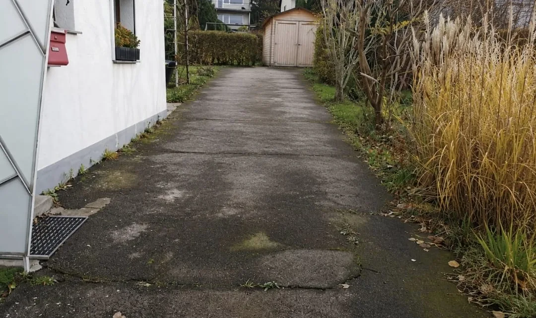 Hofzufahrt vor den Arbeiten: rissiger, bemooster Asphalt zwischen Wohnhaus und Garage