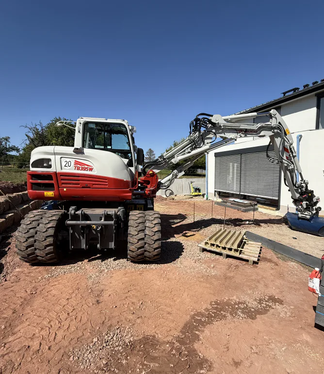 Mobilbagger von Valera steht auf dem Erdaushub vor einem Neubau mit geschlossenem Rollladen