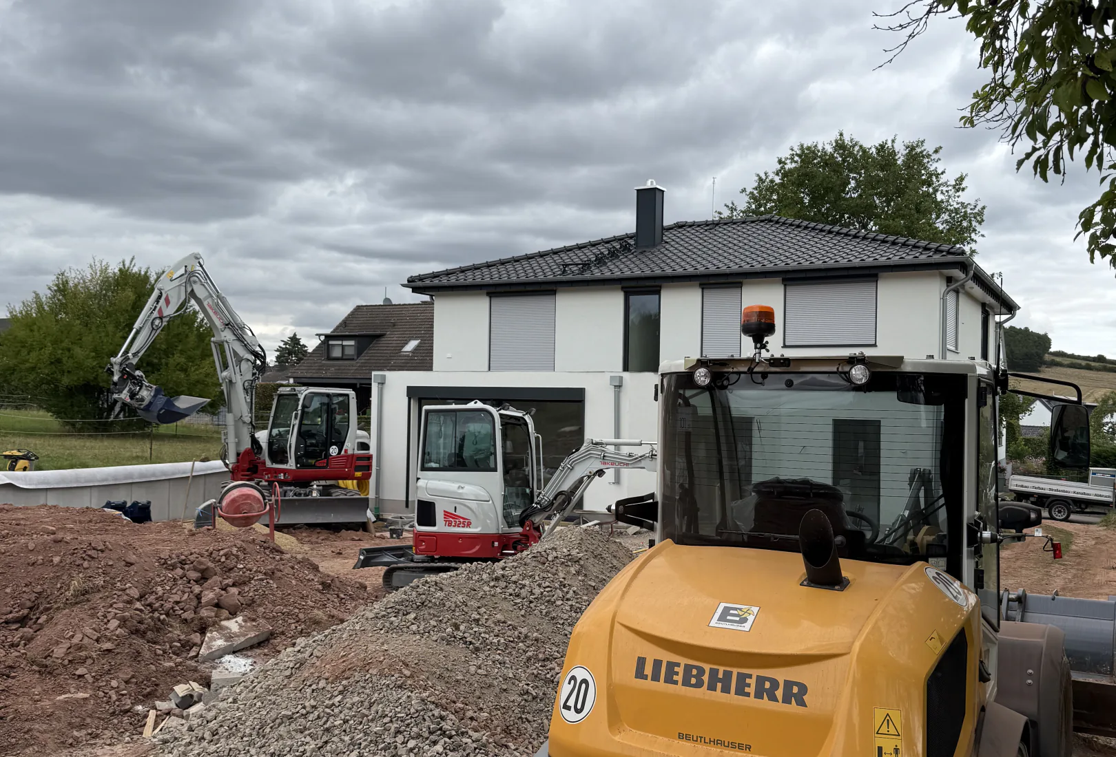Radlader und zwei Bagger von Valera auf einer Erdbaustelle vor einem fertigen Neubau